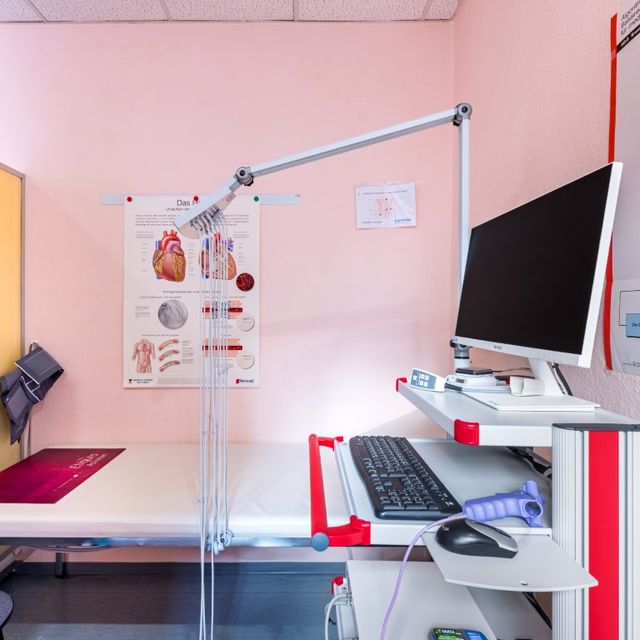 Untersuchungsraum mit Liege, Schreibtisch und Anatomie-Poster an der Wand